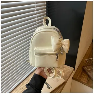 Detailansicht des cremefarbenen Mini-Rucksacks mit modischem Schleifenanhänger und Kette.