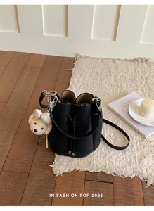 Elegant black pebble-grain bucket bag for women with cute teddy bear charm on white rug