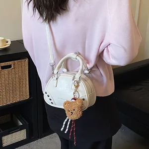 Detailed view of a white bowling handbag featuring a plush teddy bear charm on a model