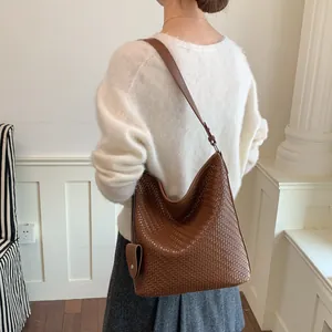 Close-up van een bruin gevlochten hobo-emmer tas op de schouder van een vrouwelijk model