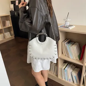 Detailed view of a white designer handbag with silver studs and chain strap in a library setting