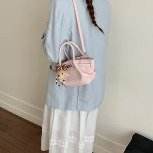 Dettaglio di una borsa a secchiello rosa con un simpatico ciondolo a orsetto su una modella.