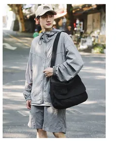 Detail view of a large black canvas messenger bag worn by a male model in a street scene