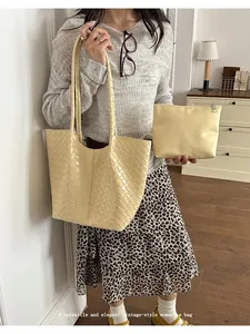 Detailed view of woven beige tote bag set with a matching pouch held by model