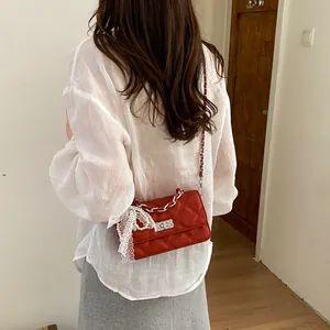 A woman wears a red quilted crossbody bag featuring a pearl and lace bow charm detail.