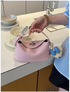 Detail view of a pink leather handbag with a swivel lock and teddy bear charm accessory