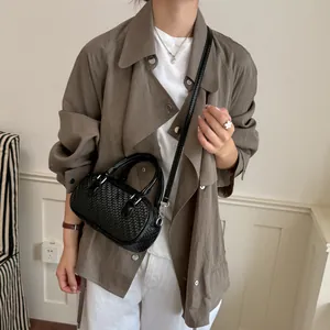 Schwarze Tasche mit Webmuster, getragen als Umhängetasche zu einer braunen Jacke