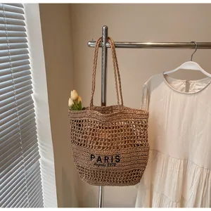 Detalle de un bolso tote de paja hecho a mano con bordado de París colgado en un soporte de metal