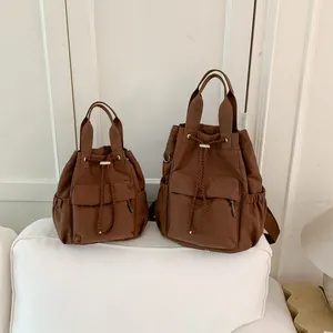 Vista detallada de dos tamaños de mochilas de nailon marrón sobre un sofá blanco