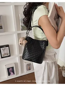 Close-up of a black woven bucket bag carried by a model in a minimal interior
