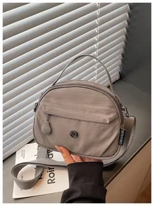 Detalle de bolso de nailon gris con logotipo CM de metal y correa ancha ajustable