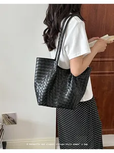 Detailed view of a black woven tote bag worn on a shoulder for a stylish look.