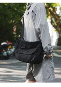 Close-up of a person wearing a large black canvas messenger bag in a sunny urban street