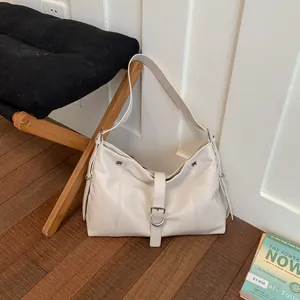 Minimalist cream leather underarm tote bag leaning against a white wall in lifestyle setting