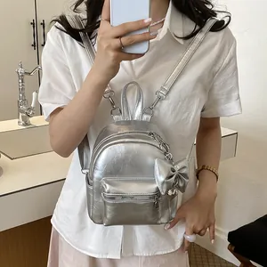Kleiner silberner Metallic-Rucksack mit Schleife, getragen von einem weiblichen Model in Innenräumen