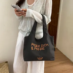 Bolso tote de lona negra con bordado naranja llevado por una mujer con estilo informal