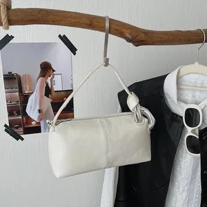 Close-up of a retro cream pillow bag with silver metal chain detail hanging on a branch