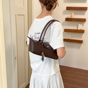 Sac à bandoulière marron foncé tendance associé à un t-shirt blanc et une jupe plissée.