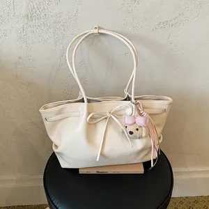 Gedetailleerde weergave van een crème tote tas met een stijlvolle strik en pluchen hondenhanger
