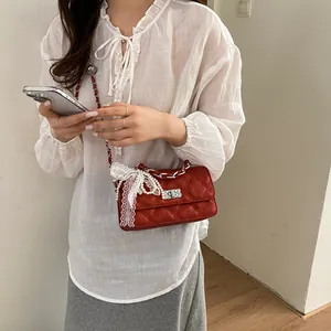 Elegant red quilted crossbody bag with lace bow and pearl chain detail worn by a model