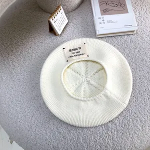 Detailed macro view of a white knitted beret with a stylish letter patch on textured surface.