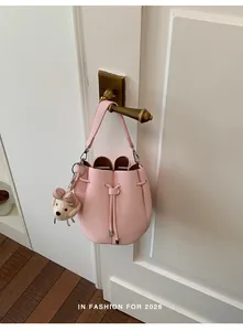 Elegant pink pebbled leather bucket bag with a cute charm hanging on a brass door handle