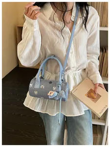 Fashionable blue denim barrel crossbody bag featuring cute cat patches and bow charm detail
