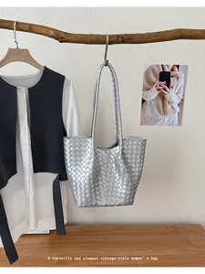 Silver woven tote bag hanging on a rustic wooden branch in an elegant interior setting.