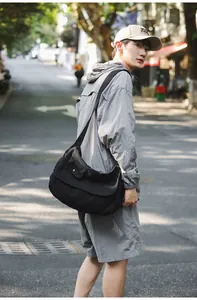 Asian male model showcasing a large black canvas messenger bag in a casual urban street
