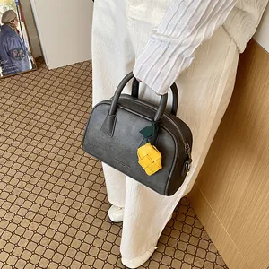 Close-up detail of a dark grey textured pillow bag held by model with a yellow woven charm