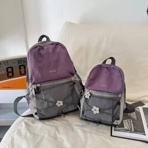 Zwei leichte Rucksäcke in Lila und Grau im Set zum Größenvergleich auf einem hellen Sofa.