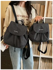 A stylish woman showcases a small black and white grid-patterned backpack in a library