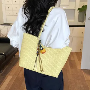 Bolso tote tejido amarillo pálido al hombro, que muestra textura y detalles del diseño.