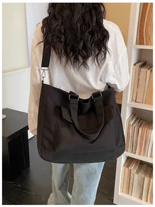 Detail shot of a large black canvas tote bag worn as a casual crossbody for travel.