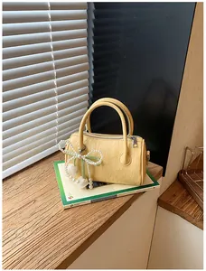 Elegant yellow textured pillow handbag with a pearl bow charm on a decorative book