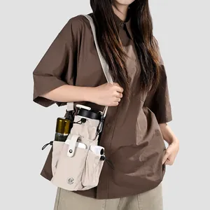 Détail d'un sac bandoulière en nylon crème avec poches pour bouteille et téléphone.