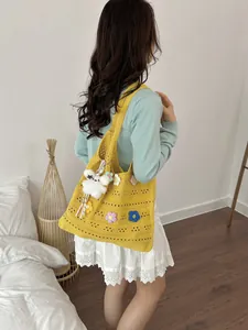 Detailansicht einer gelben handgehäkelten Tragetasche mit Blumendekor und süßem Anhänger.