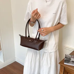 Vue détaillée d'un sac baguette en cuir marron minimaliste porté par un mannequin femme.