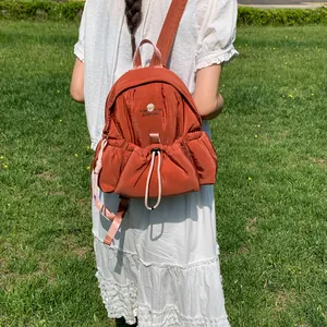 Mochila terracota con bolsillo de cordón mostrada en modelo en un entorno de césped.