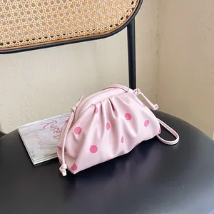 Pink polka dot pleated cloud bag displayed on a stylish black designer chair.