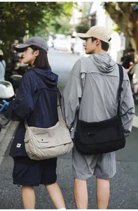 Two models wearing minimalist large capacity canvas messenger bags in a street setting