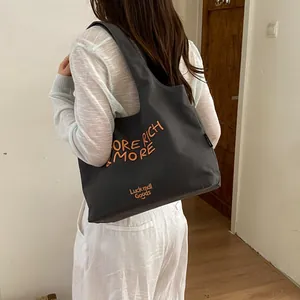 Detalle del gran bolso tote de lona gris con bordado naranja llevado por el modelo