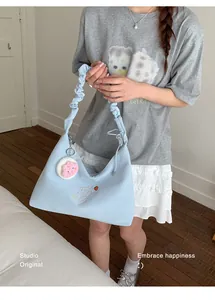 Detalle de bolso de hombro azul claro con asa plisada y bordado de fresa en escena diaria