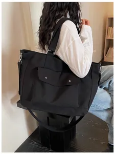 Large capacity black canvas tote bag with front pocket shown on a model for travel and daily use