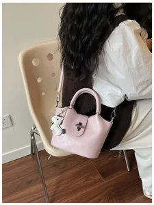 Détail d'un sac à main seau rose avec verrou métallique et breloque cheval blanc.
