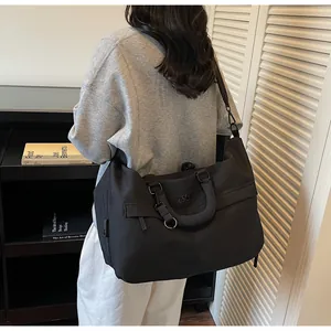 Détail d'un grand sac de voyage noir porté par une femme dans un intérieur moderne