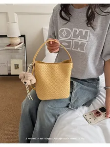 Detailed view of a yellow woven vintage-style bucket bag with a cute bear charm