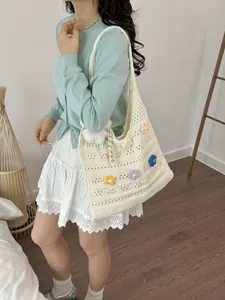 Detailansicht einer cremefarbenen, handgestrickten Tragetasche mit bunten Blumenakzenten