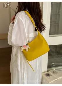 Close-up detail of a minimalist yellow leather underarm bag featuring a cute horse charm
