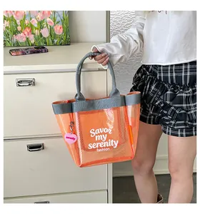 Detail view of stylish orange mesh handbag with slogan and heart-shaped charm